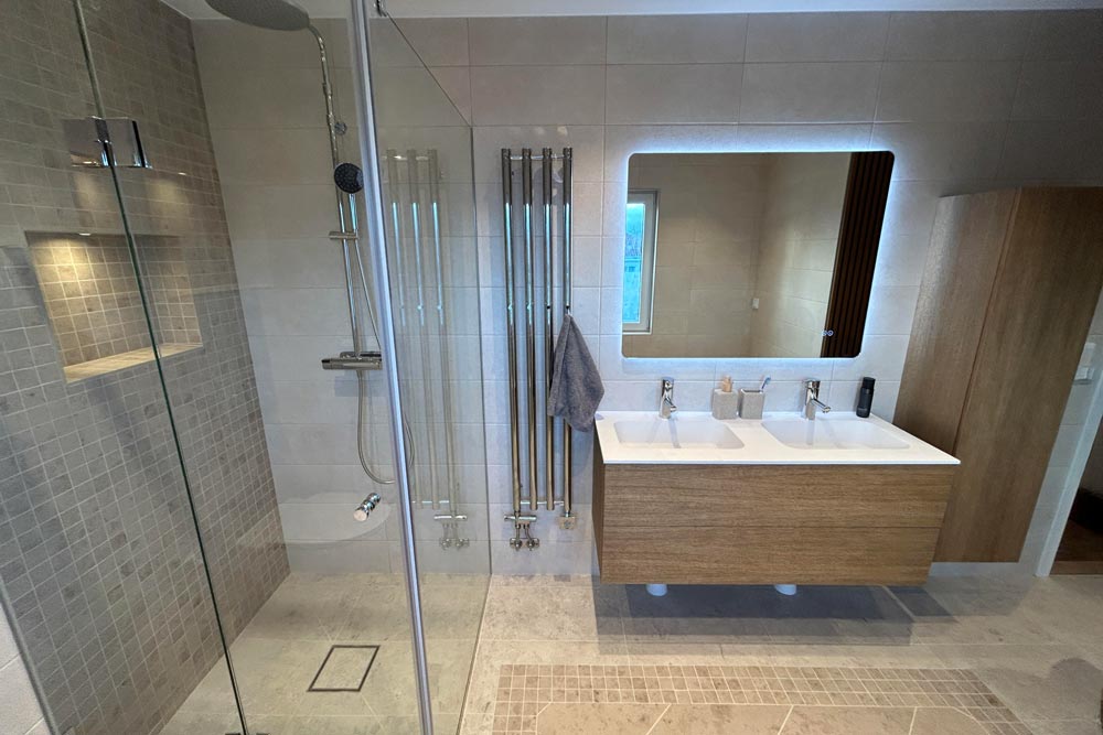 Ett ljust kaklat badrum med en lysande väggspegel