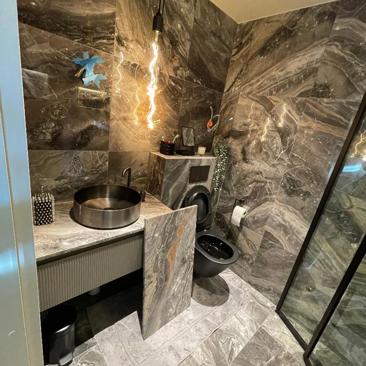 Ett badrum med grått kakel och en svart toalett