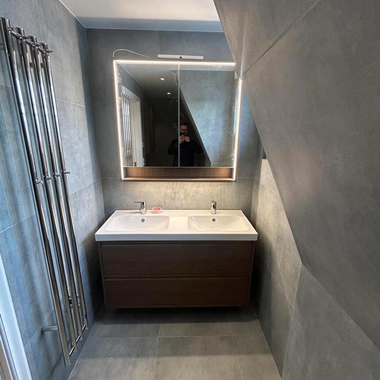 Ett badrum med grått kakel och en stor väggspegel