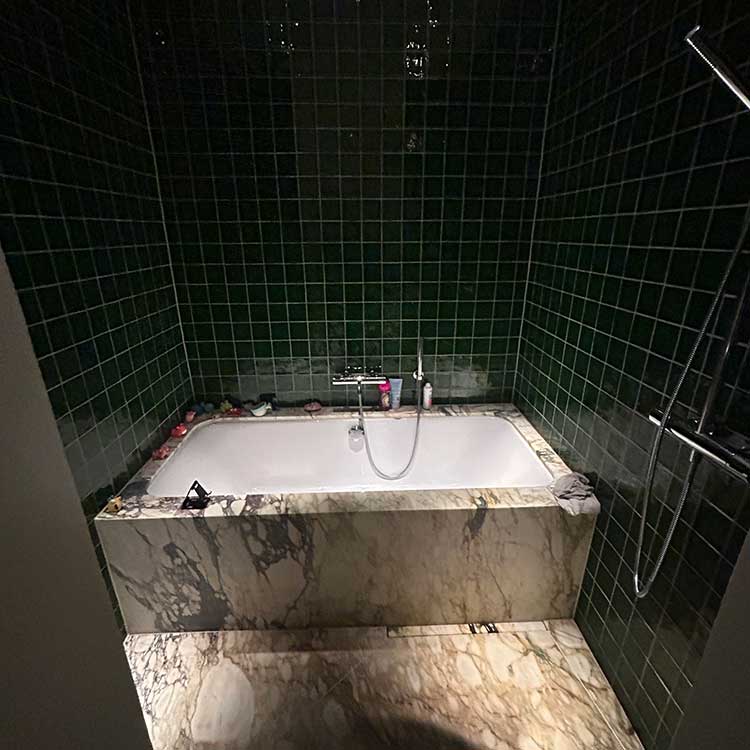 Modernt badrum med gröna väggar och marmor i golv, badkar och handfat